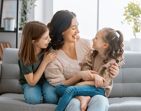 Mother With Two Young Children, Sitting On Couch And Laughing